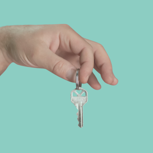 lave de casa colgando en mano sobre fondo azul Llave metálica de casa colgada en un llavero, sostenida por una mano sobre fondo azul